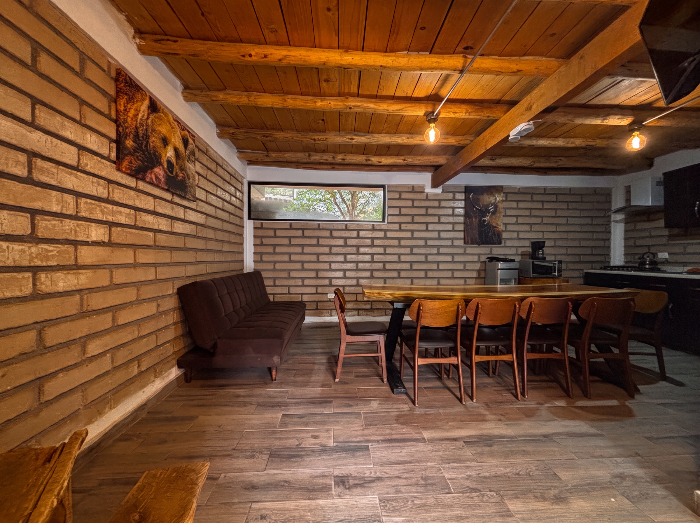 Comedor amplio de ANDROMEDA con sillones, vigas de madera y muros de ladrillo rústico