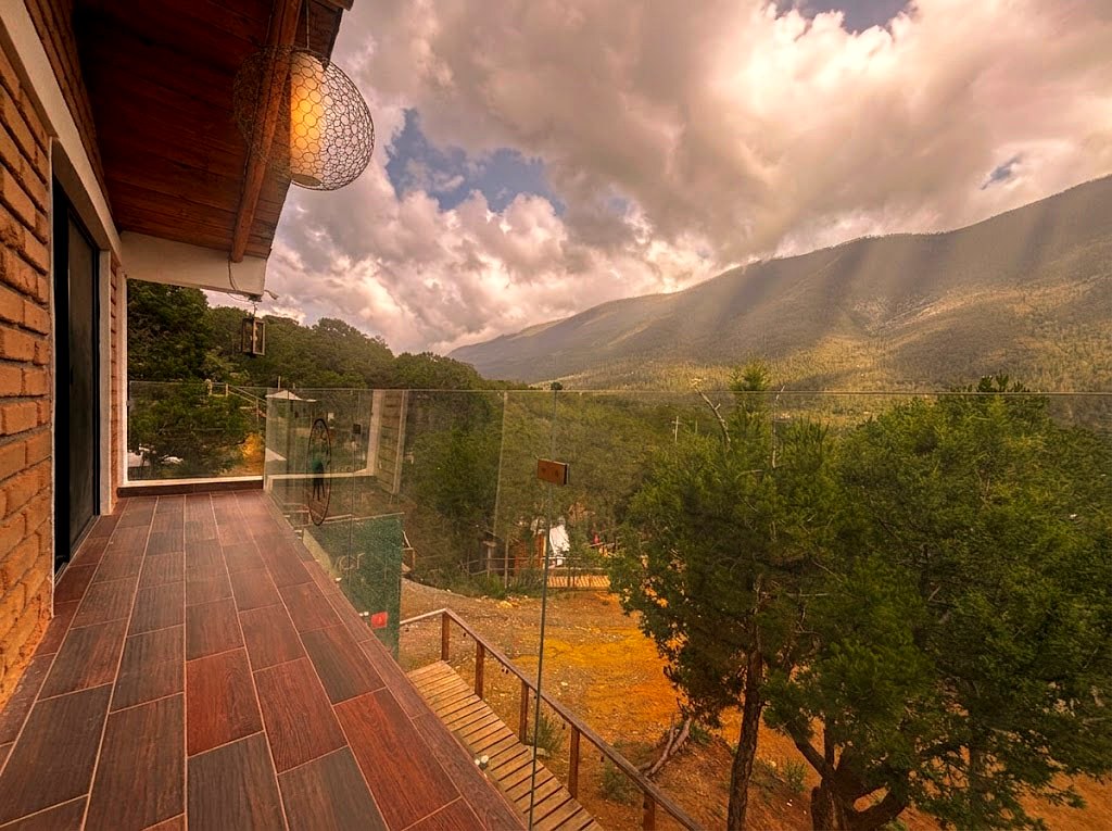 Terraza de OSA MAYOR con piso de madera, barandal de cristal y vista panorámica a la Sierra de Arteaga entre nubes