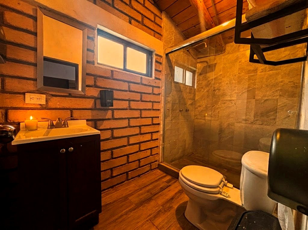 Baño completo de OSA MAYOR con regadera de cristal, paredes de ladrillo y acabados en madera