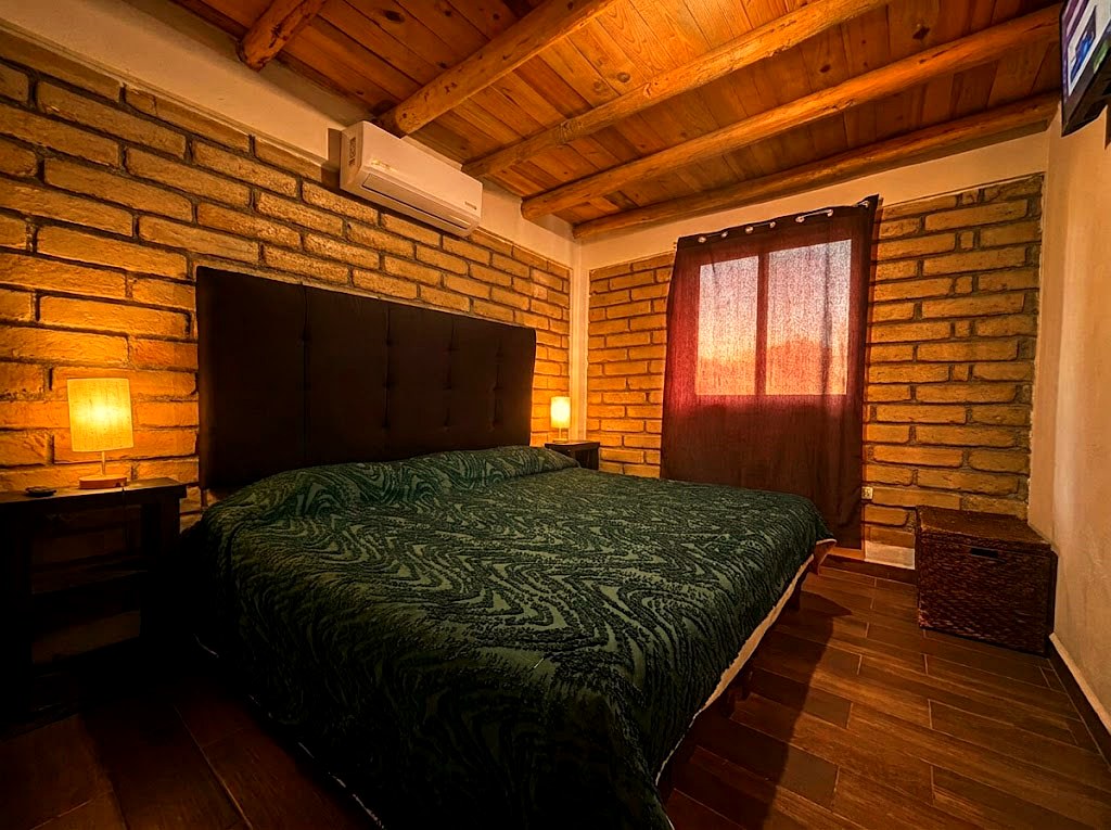 Recámara de planta baja en OSA MAYOR con cama king, paredes de ladrillo y lámparas cálidas