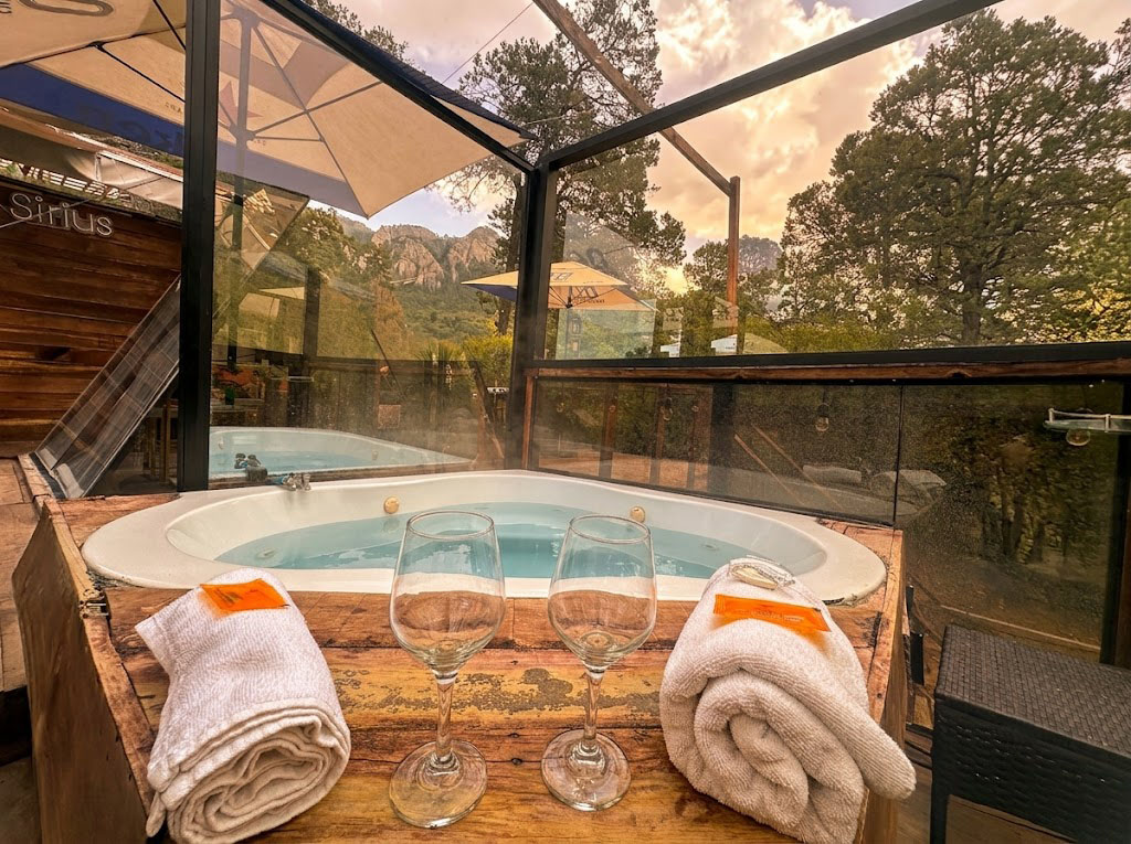 Jacuzzi privado de SIRIUS con copas, toallas y vista panorámica a la sierra a través de ventanales de cristal al atardecer