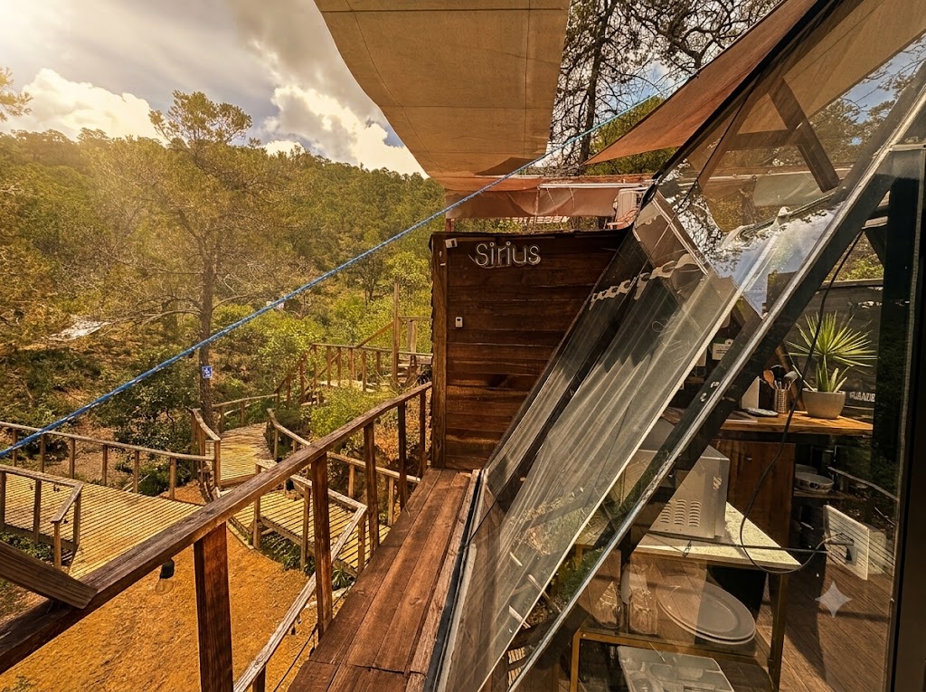 Vista lateral de SIRIUS con letrero de madera, deck elevado y ventanales de cristal integrados al bosque