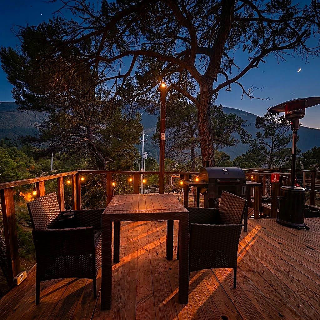 Terraza privada de ALTAIR con mesa, sillas, asador y luces cálidas bajo un cielo azul de atardecer