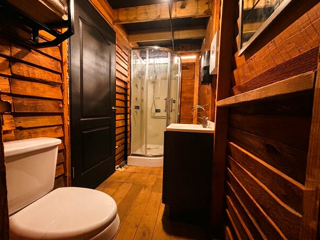 Baño de FENIX con regadera hidromasaje de cristal, lavabo, sanitario y muros de madera rústica