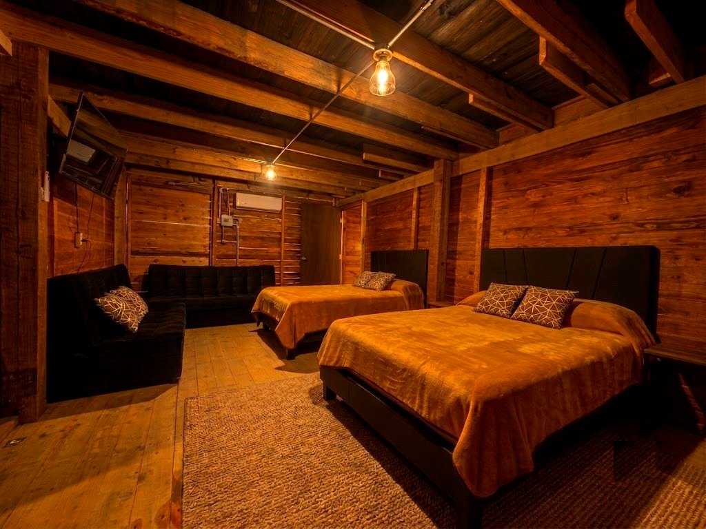 Recámara principal de FENIX con cama king y cama matrimonial, sofá cama, Smart TV y muros de madera cálida