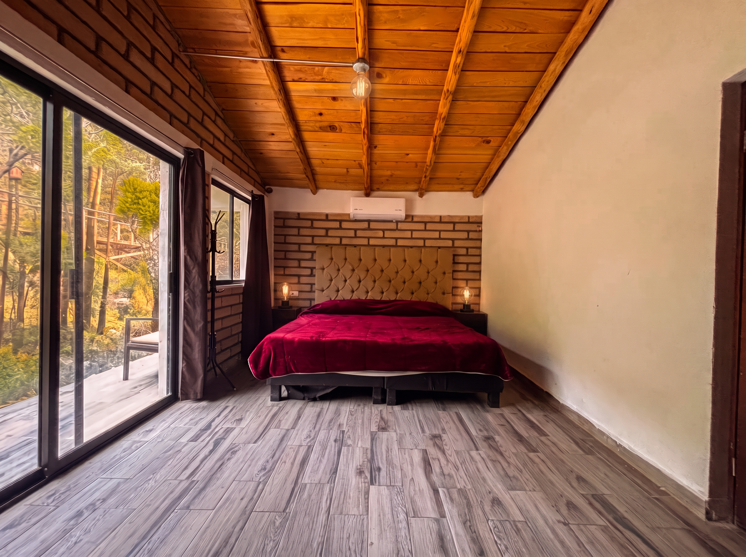 Recámara principal de ANDROMEDA con cama king, techo de madera y ventanal con salida a terraza al bosque