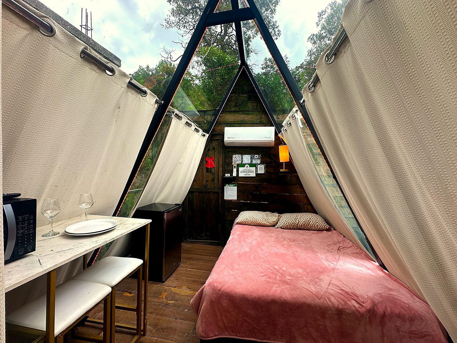Interior de AURORA BOREAL con cama matrimonial, cocineta, cortinas texturizadas y climatización bajo el techo A-frame