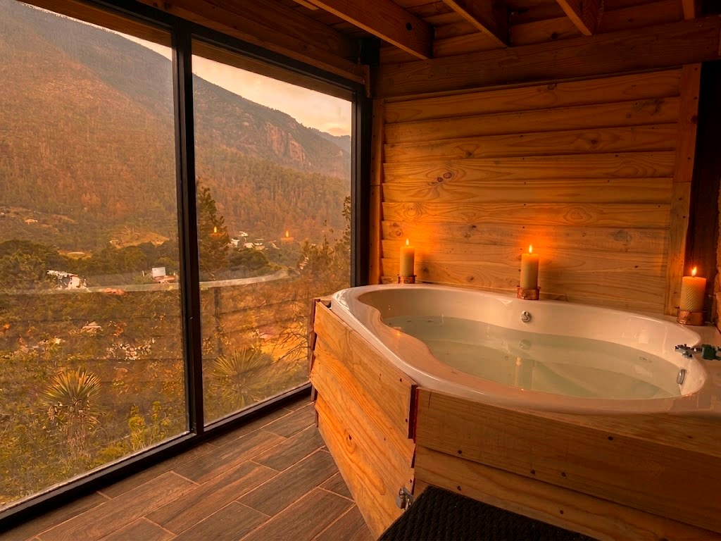 Jacuzzi privado de ORION junto a ventanal panorámico con velas encendidas y vista a la sierra al atardecer