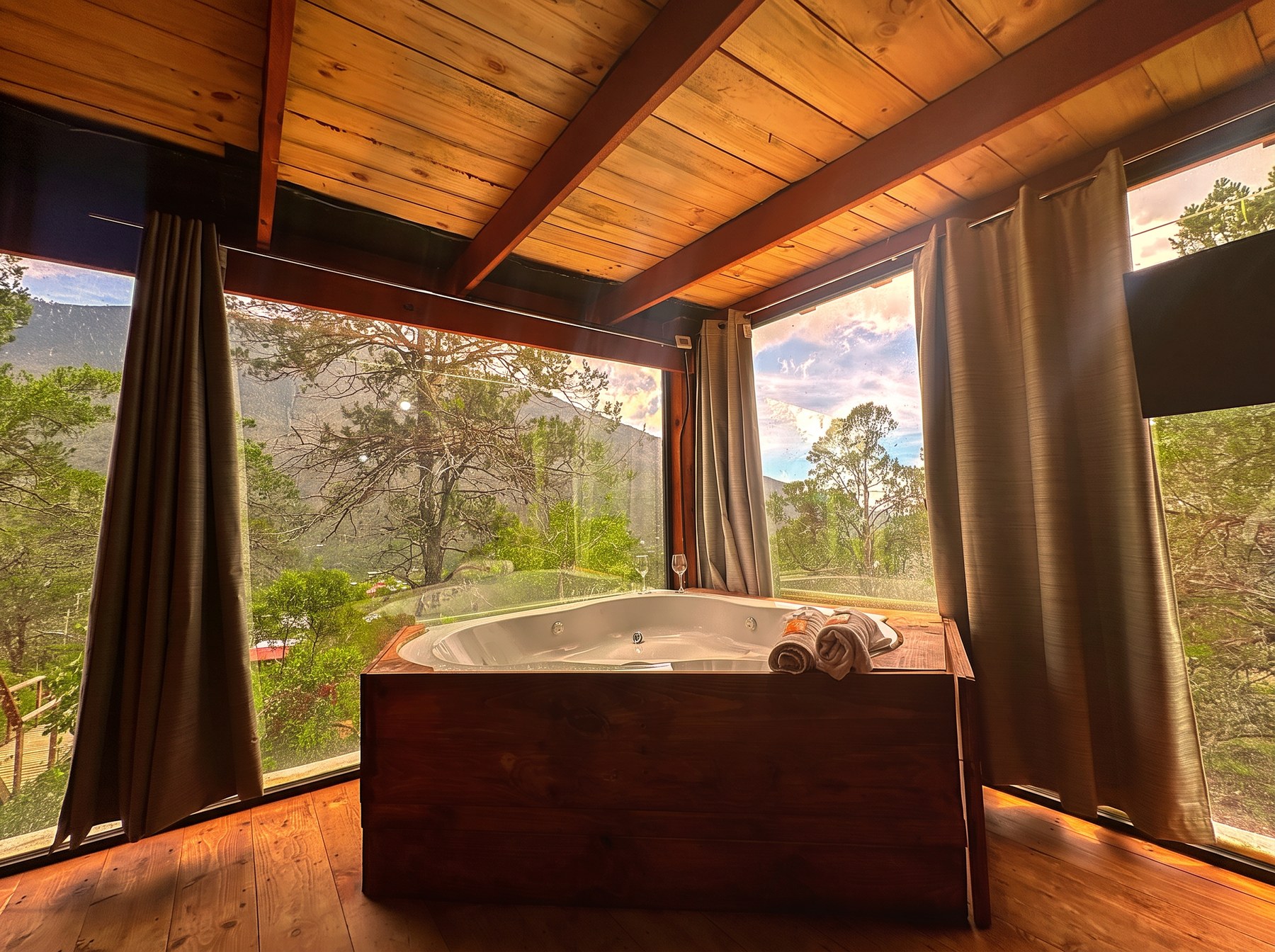 Jacuzzi de ATENEA bajo techo de madera con ventanales de cristal y vista al atardecer en la Sierra