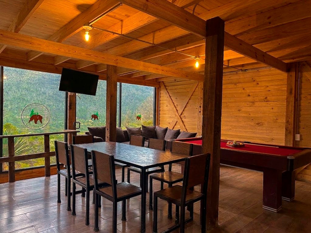 Sala común de ORION con sofá tipo chesterfield, mesa de tronco natural, Smart TV y ventanales al bosque