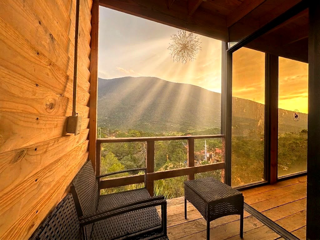 Terraza privada de ORION con sillones de exterior, vista panorámica a la montaña y rayos de sol filtrándose