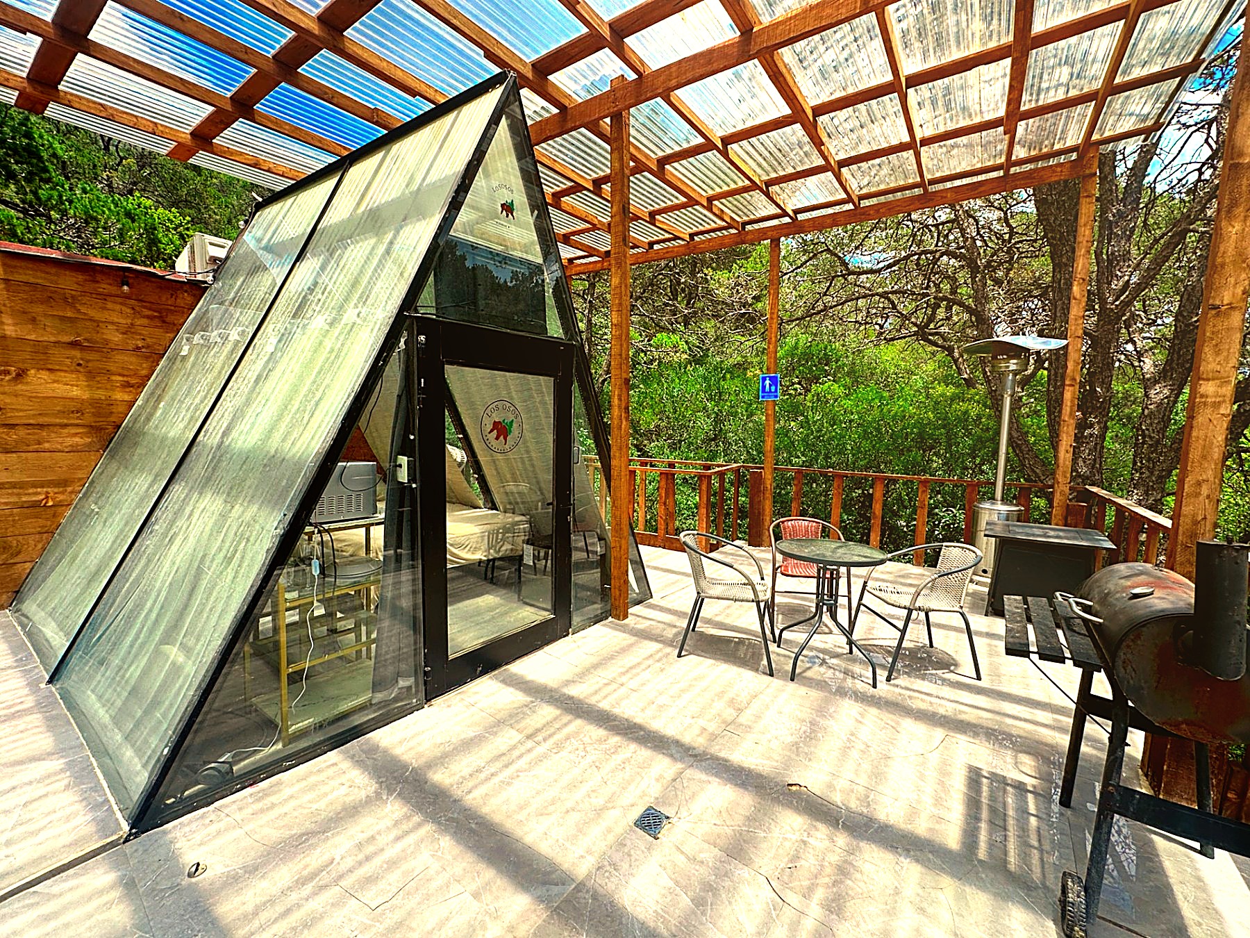 Terraza privada de ATENEA con estructura A-frame de cristal, asador, calentador de patio y mesa entre los pinos