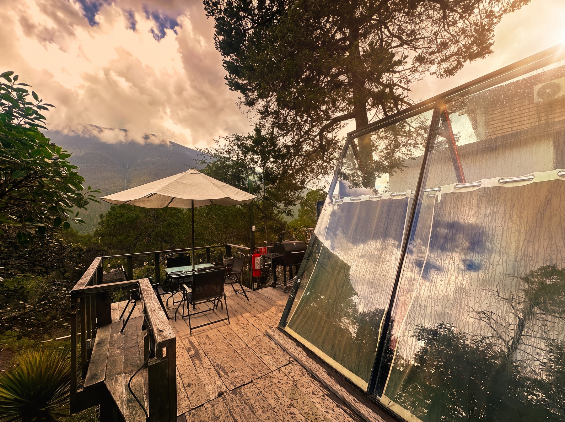 Terraza de AURORA BOREAL con vista panorámica a la sierra entre nubes, deck de madera y ventanales del A-frame de cristal